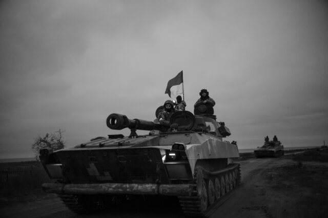 A Tank waving the Ukrainian flag with military on top entering Oleksandrivka at night.