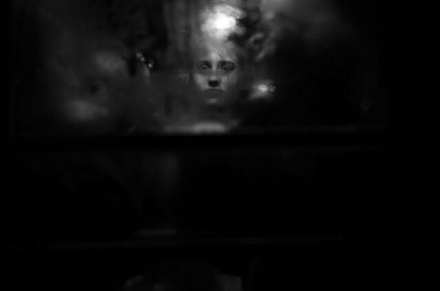 woman in the dark looking through window in train at the lens.