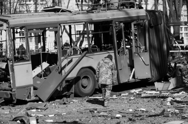 A destroyed bus after attacks on the city, rubble and debris everywhere, a man in military clothing inspects the damages, Kyiv , Ukraine - 14/03/2022