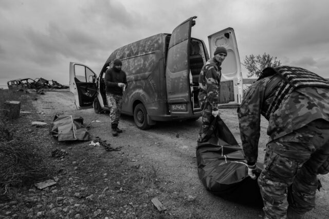 Two soldiers, military carry human remains in a body bag into a vehicle, van. body bags marked for soldiers and unmarked for civilians have been prepared by Ukrainian forensic teams for collection by 