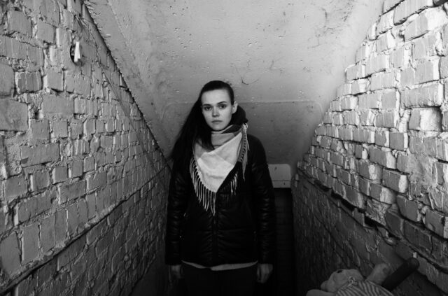 Portrait of a young woman in front of the entrance of a basement she was forced to live in during Russian occupation of her village.