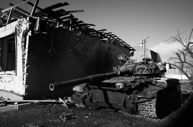 A destroyed tank next to a half destroyed building in a conflict area