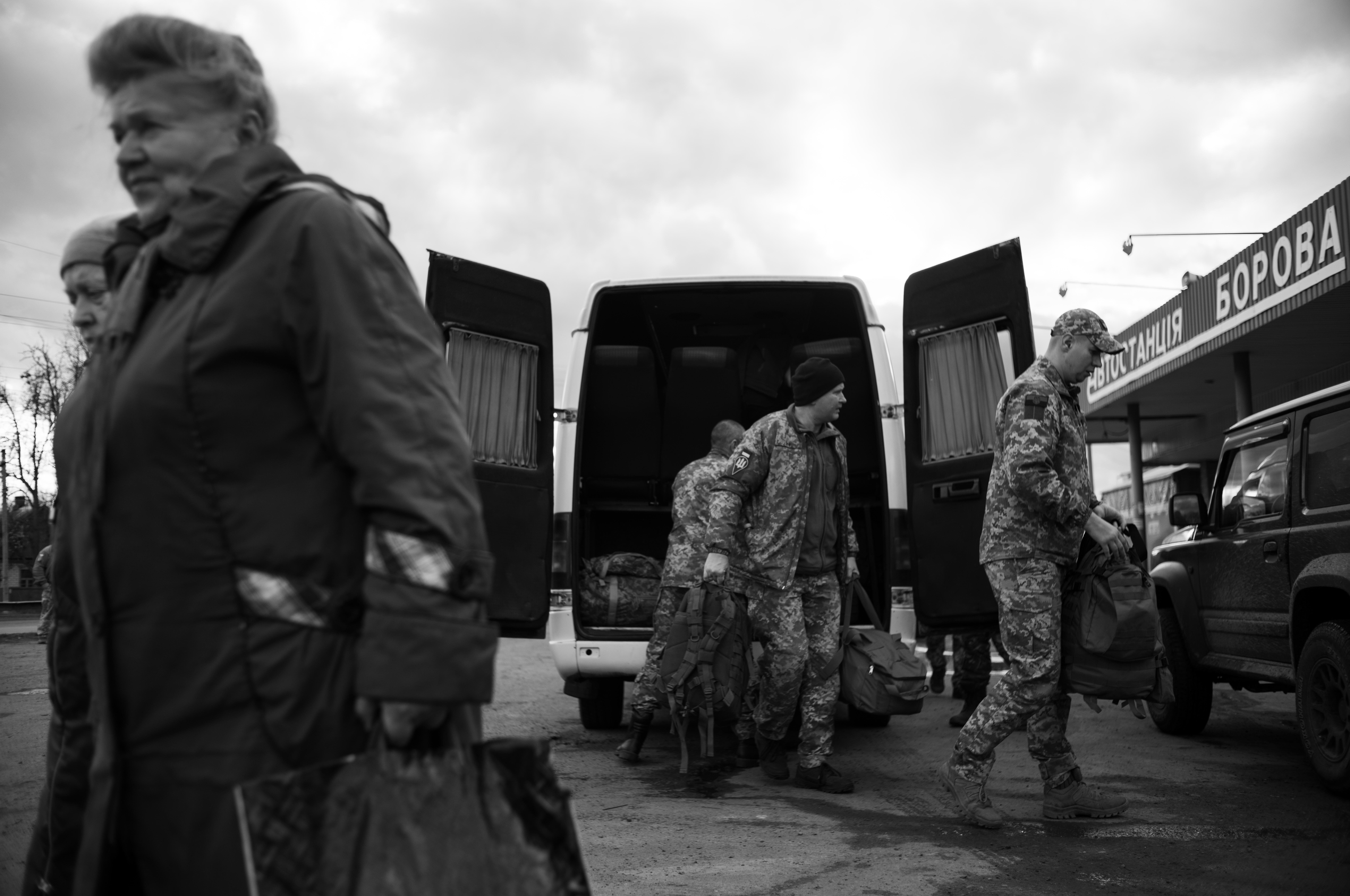 Borova, Kharkiv region, Ukraine, 2023 – Civilians and military personnel spill out from arriving buses and minibuses, grabbing their backpacks and trunks from the luggage compartments. They disappear silently and attentively onto military vehicles or on foot.