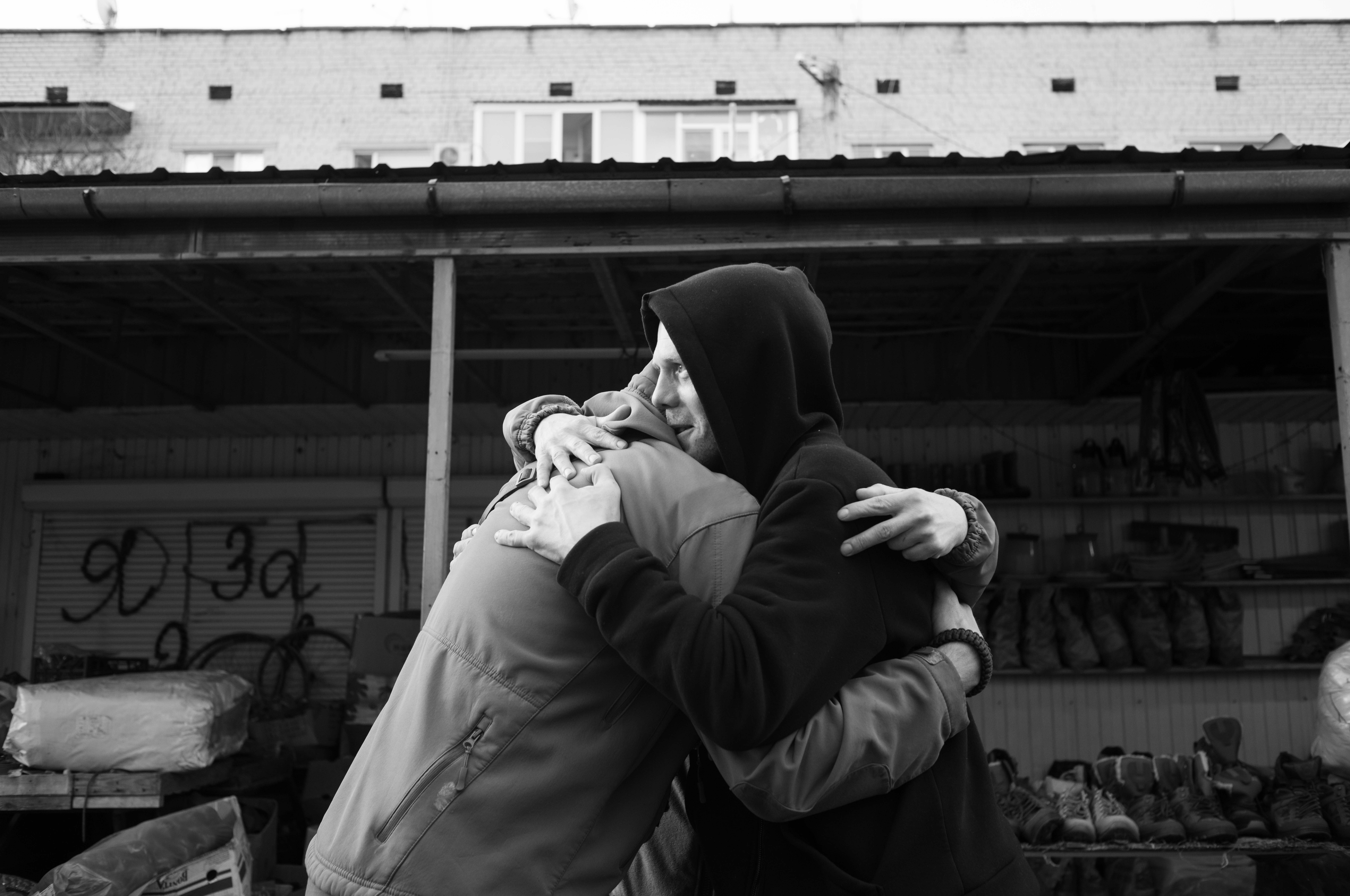 Borova, Kharkiv region, Ukraine, 2023 – In the midst of the market stalls filled with cheap military gear near the bus station, two men embrace—a pair clearly military, though one in civilian attire, having recovered from an injury. The one in pixels, Sergiy, aged forty, a platoon commander, has spent four consecutive days in the trenches at the front line. As he holds his comrade, his shoulders begin to tremble.